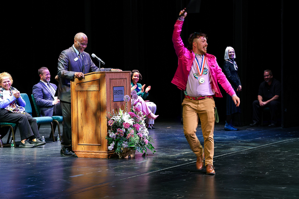 A student excited to receive their award at Student Awards Night. Bristol President Harris and staff members smile as the student walks the stage.