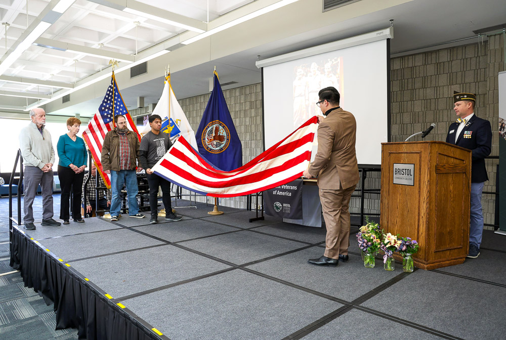 Two people on stage folding a flag at Bristol Community College's Veterans Day Ceremony.