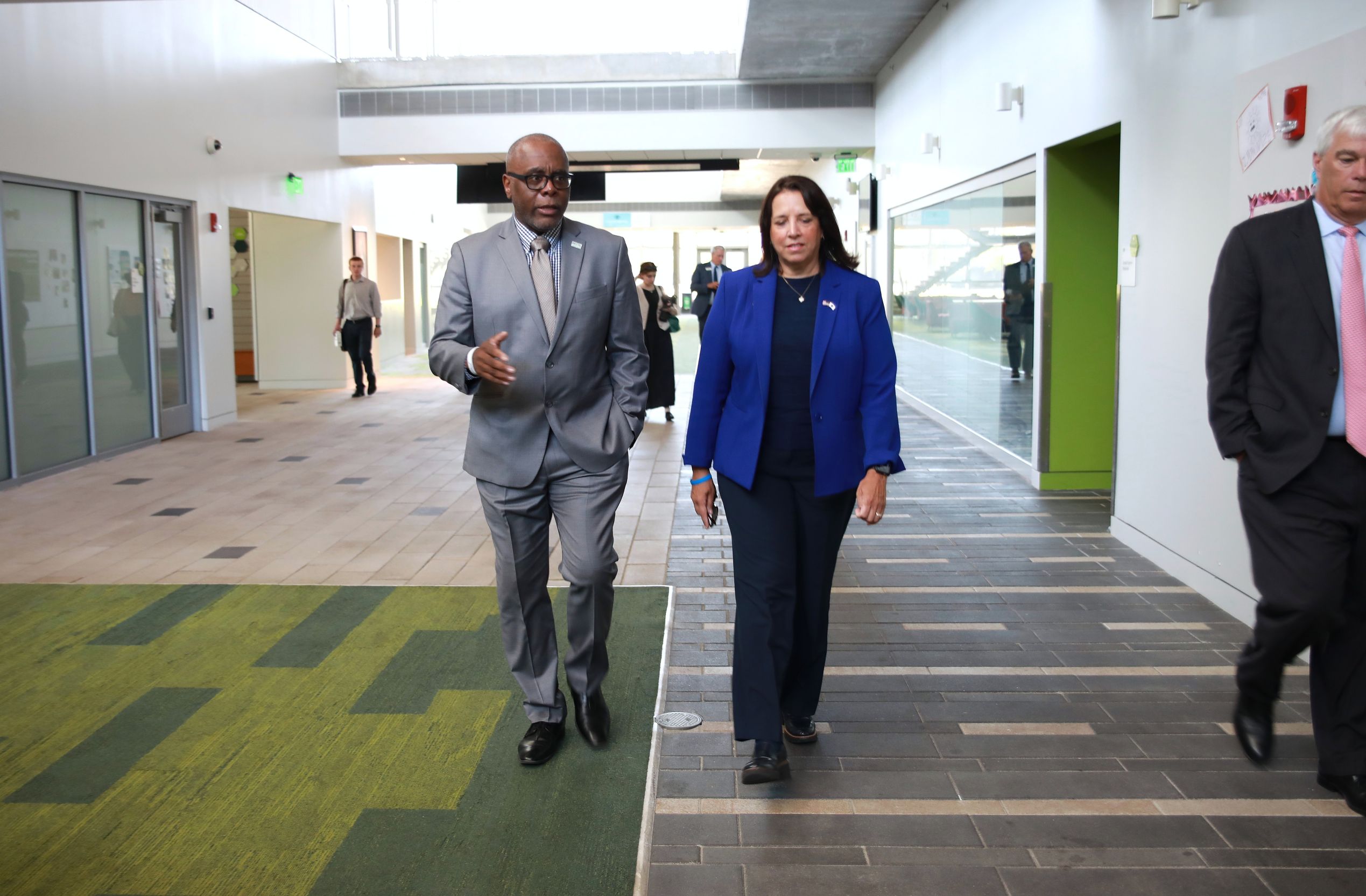  Two men and a woman walking together down a well-lit hallway, engaged in conversation.