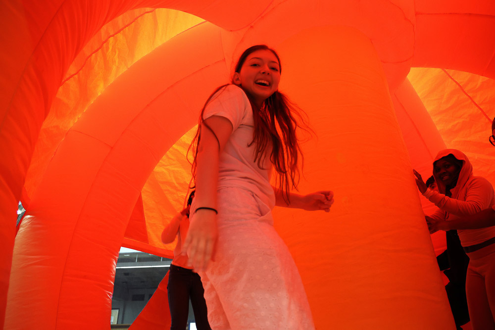Student having fun at a campus event in an inflatable house. There is an orange glow coming from the house on the participants.