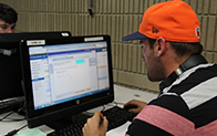 student wearing orange baseball cap and doing work on computer