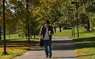 student holding coffee walking on campus sidewalk