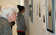 person with white hair and glasses views art work hanging on a wall