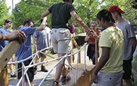person being helped across rope and wood bridge